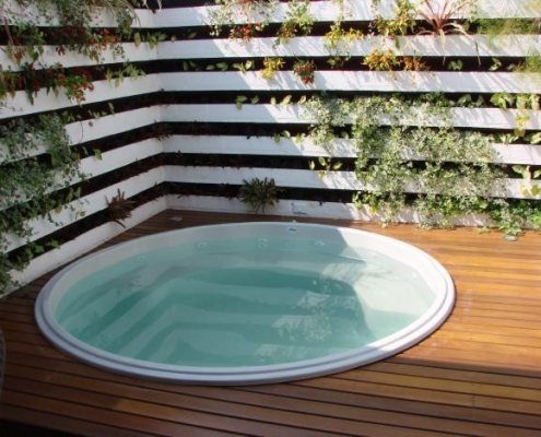 Piscina em fibra de vidro redonda em deck de madeira, com jardim suspenso em parede de madeira branca.